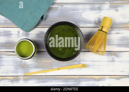 Top down view on white wood table with chawan bowl, bamboo whisk and spoon, can green matcha tea powder and blue napkin Stock Photo