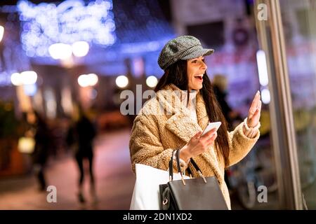 Pretty young woman with mobile phone by the shop window at Christmas time Stock Photo