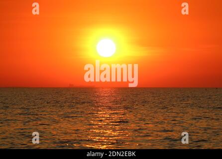 Bright sun on the orange sky setting over the sea Stock Photo