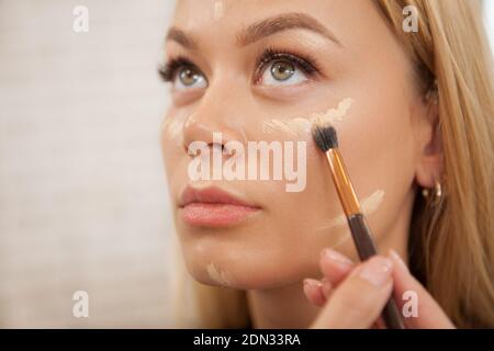 Close up of a makeup artist applying liquid concealer or highlighter on the face of female client Stock Photo