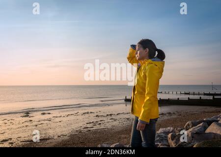 Mature woman wearing a yellow jacket, looking out to sea. Alone concept. Stock Photo