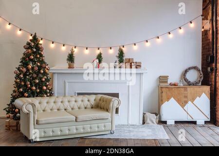 Christmas decor. Bright interior of a white sofa, decorative Christmas tree, fireplace and garland, New Year eve Stock Photo