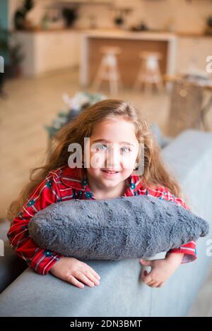 cute girl portrait. Little girl in red pajama smiling at home n the gray sofa Stock Photo