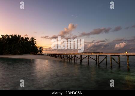 Wooden jetty with lanterns over the ocean extending from tropical island, with blurred water and sunset in the background, Maldives, long exposure. Stock Photo