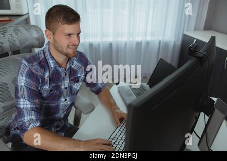 Cheerful male program developer working on his computer at home. IT industry freelancer enjoying working on a project Stock Photo