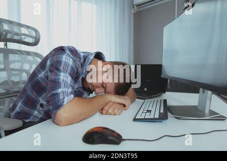 Handsome male freelancer sleeping on the desk in front of the computer, copy space. Male student sleeping on the table with computers after studying Stock Photo