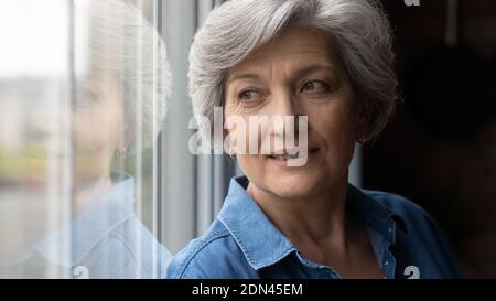 Happy middle aged woman dreaming near window. Stock Photo