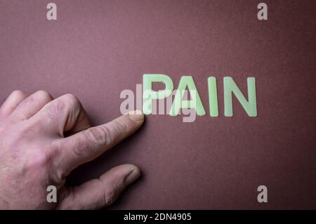Human fingers pointing the word Pain written with plastic letters on brown paper background, concept Stock Photo