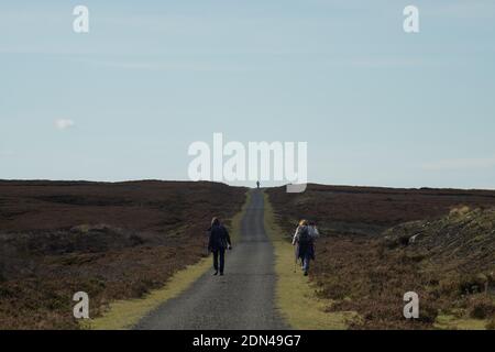 Two female walkers heading along the Waskerly Way moorland path with a single walker outlined on the distant horizon forming a strong triangular shape Stock Photo