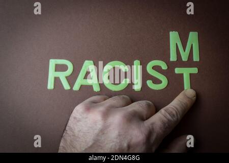 Human fingers sliding a letter to the word Racism to make it Racist, written with plastic letters on a brown paper background, concept Stock Photo