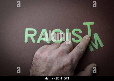 Human fingers sliding a letter to the word Racism to make it Racist, written with plastic letters on a brown paper background, concept Stock Photo