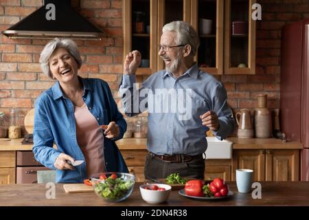 Emotional middle aged family couple having fun preparing food together. Stock Photo