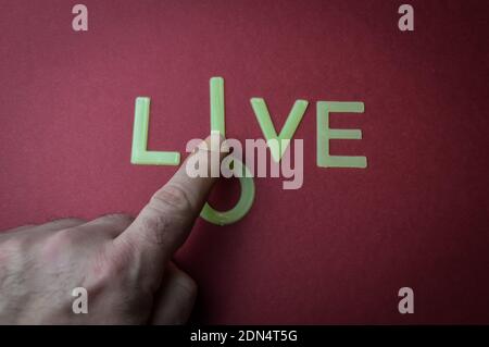 Human fingers sliding a letter to the word Love to make it Live, written with plastic letters on a dark red paper background, concept Stock Photo