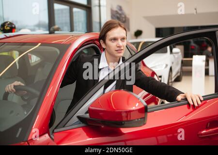 Young man choosing new car to buy at the dealership. Businessman buying new auto, getting into the vehicle Stock Photo
