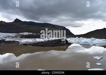 The Svínafelljokull glacier as it flows into the glacial lagoon in Vatnajokull National Park, Iceland. Reflection of surrounding mountains in the lake. Stock Photo