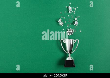 Winner or champion silver trophy cup with confetti on green background top view. Winning or success concept.