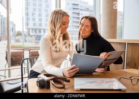 Young Female Blogger Colleagues Discussing Over Magazine At Restaurant Stock Photo