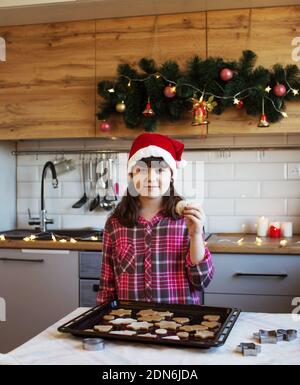 The girl in the kitchen is standing next to a tray of cookies Stock Photo