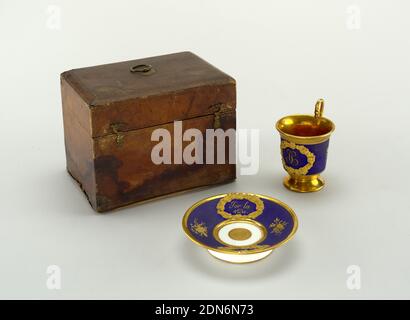 Traveling case with cup and saucer, Stamped and dyed leather adhered to wood, cast brass (case); enameled, glazed and gilt porcelain, blown and engraved glass, Cup with flaring rim, high loop handle terminating in a serpent's head, with high foot. Ornamented with trophies and initials 'T.C.' in raised floral wreath. Foliate bands near rim and base of cup. Saucer decorated with trophies and raised floral wreaths, one with inscription 'Por la vida', the other with pair of blazing hearts. At center of bowl, circular medallion with five-pointed star. Rectangular leather-covered case Stock Photo