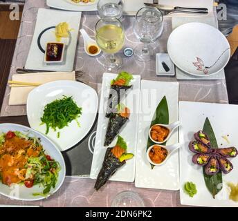 Japanese flat lay on a table full of delicious dishes. Uramaki of shrimp tempura, Temaki rice cones, fresh salmon tartar, seaweed with soy sauce Stock Photo