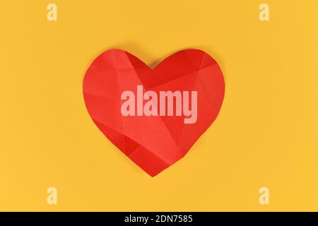 Red paper heart with folding lines on yellow background. Concept for broken or sick heart Stock Photo