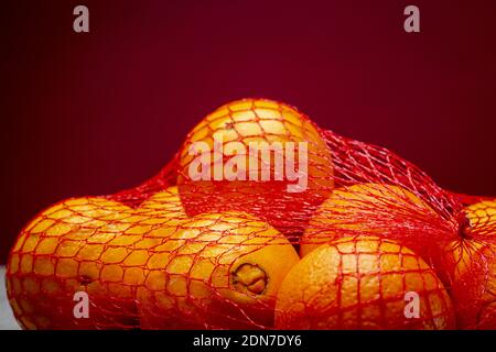 Closeup of a bunch of oranges in red carrying net on a textured kitchen surface and dark purple background Stock Photo