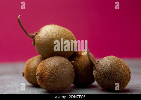 Bunch of tiny kiwifruit of Actinidia Deliciosa Setosa species with stems sticking out on metal kitchen surface against a purple out of focus back Stock Photo