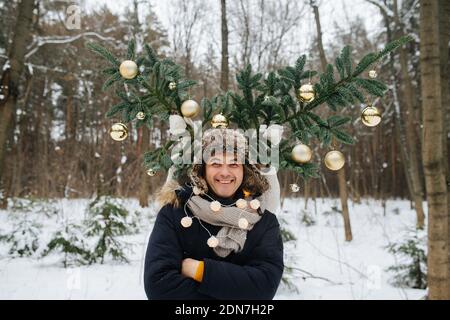 A wife makes horns of Christmas tree for her husband, she hiding behind him Stock Photo