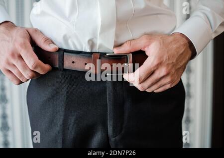 Men's Accessories. The man puts on a brown leather belt. Male hands close up Stock Photo