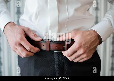 Men's Accessories. The man puts on a brown leather belt. Male hands close up Stock Photo