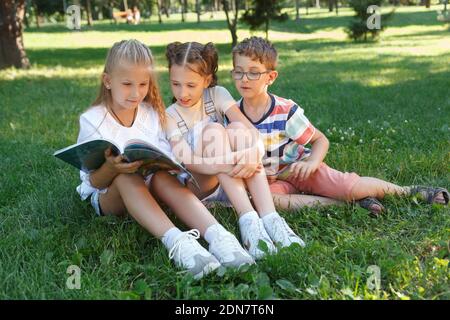 Three children reading a book together on the grass at the park Stock Photo