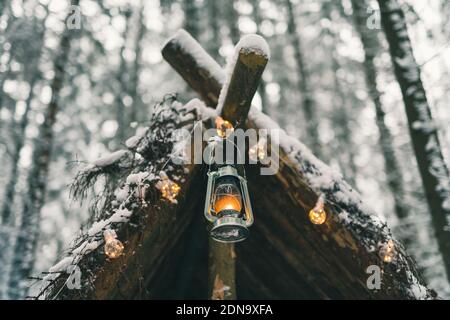 Kerosene lamp and garlands hanging on survival shelter in winter forest Stock Photo