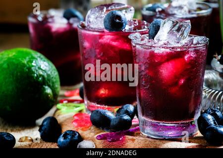 Alcoholic cocktail Darkside, with liqueur, blueberry, lime juice, crushed ice, bar tools on a vintage wooden background, selective focus Stock Photo