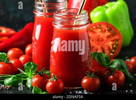 Spicy tomato juice with chili, bell peppers and green basil in glass bottles on black background, selective focus Stock Photo