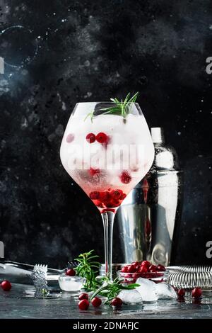 Cranberry cocktail with ice, fresh rosemary and red berries in big wine glass, bar tools, gray bar counter background, copy space, selective focus Stock Photo