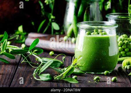 Cream soup from green peas in glass jar on vintage wooden background, selective focus Stock Photo
