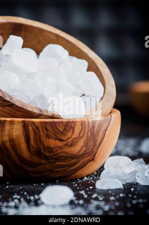 White crystal candy sugar in wooden bowl on black table, selective focus Stock Photo