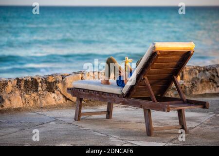Person from the back laying on lounge beach chair looking at the ocean tropical paradise Stock Photo