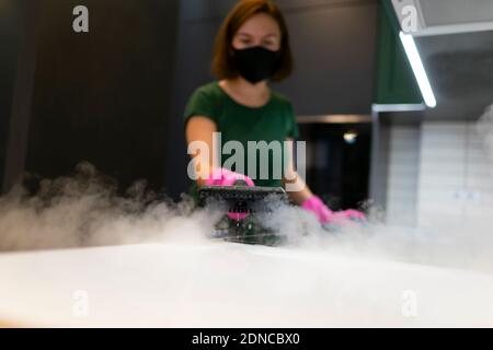 Woman employee cleaning company blows vapor out of steam generator. Steam cleaning process for kitchen furniture Stock Photo