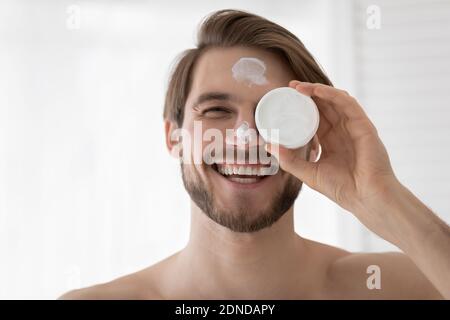 Happy young handsome man applying moisturizing cream. Stock Photo