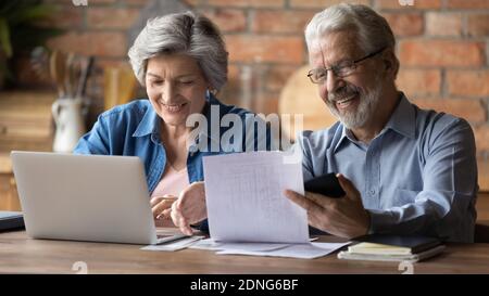 Happy old mature married couple calculating domestic utility bills. Stock Photo