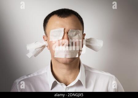 A man with eyes, mouth and ears sealed with painting tape. A concept on the topic of fear of telling the truth. Stock Photo