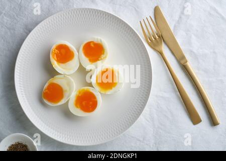 Soft-boiled eggs, peeled and cut into two halves, lying on white plate Stock Photo