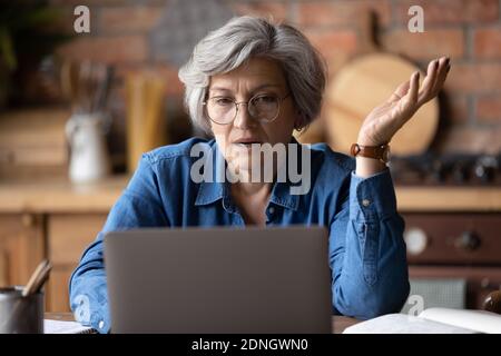 Confused middle aged woman in glasses looking at computer screen. Stock Photo