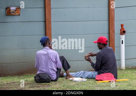 Alberton, South Africa - homeless unemployed black men eating food sitting on a pavement image in horizontal format Stock Photo