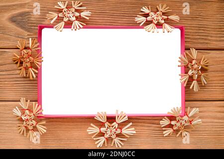 The white rectangle is surrounded by straw snowflakes. Warm wood background. Stock Photo