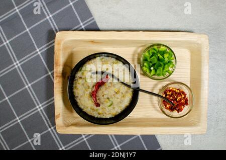 Cooked Dalia in Black Bowl, capsicum  and red chilli flakes in  glass bowl. Bulgar wheat, Broken wheat or cracked wheat or couscous is made by milling Stock Photo