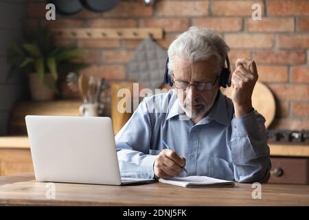 Focused middle aged man in headphones studying on online courses. Stock Photo