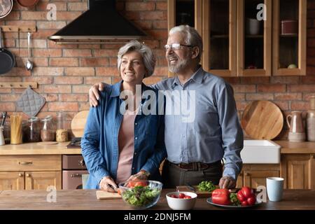 Happy middle aged family couple dreaming, distracted from preparing food. Stock Photo