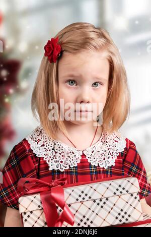 A little girl in a red dress holds a gift box in her hands. Christmas card. Stock Photo